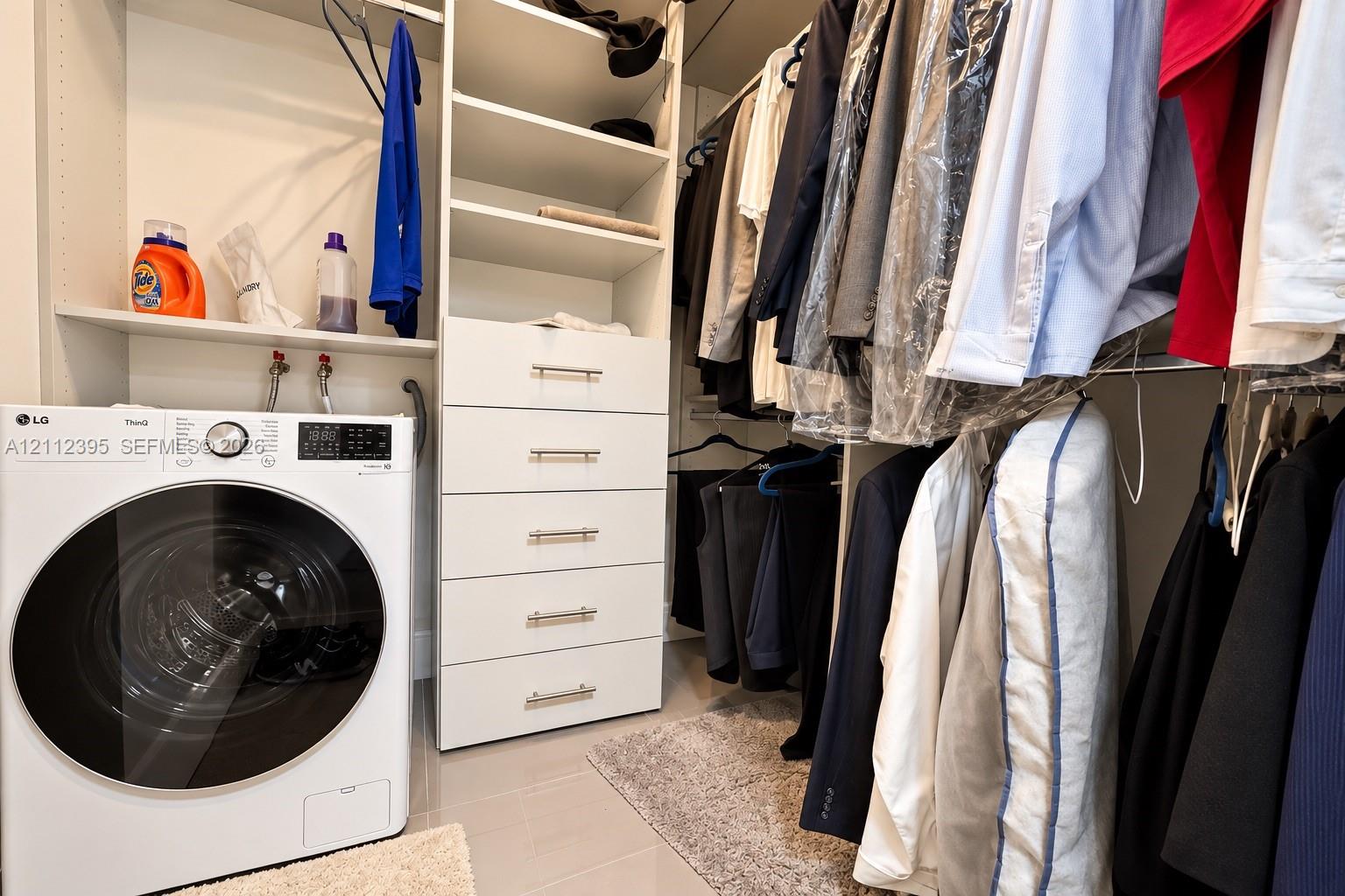 Walk-in closet featuring white built-in shelving, a five-drawer dresser unit with metallic pulls, and an integrated laundry space with a front-loading washing machine