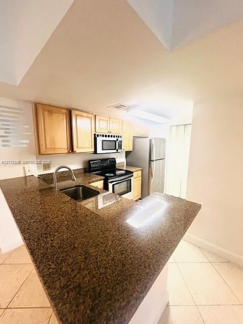Kitchen featuring natural-finish cabinetry, stone-surface countertops, an undermount stainless steel sink, a stainless steel range, and tile flooring Kitchen featuring natural-finish cabinetry, stone-surface countertops, an undermount stainless steel sink, a stainless steel range, and tile flooring
