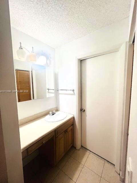 Built-in wooden vanity with countertop sink, ceramic tile flooring, three-light vanity fixture, and wall-mounted mirror