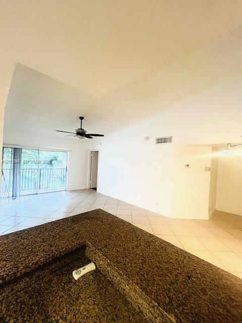 Stone-surface breakfast bar featuring a deep-set counter, tiled flooring, vaulted ceiling, and sliding glass doors with balcony access