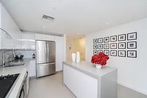 Modern kitchen featuring high-gloss cabinetry, a central island with a solid surface countertop, stainless steel appliances, and a polished sink with a curved faucet Modern kitchen featuring high-gloss cabinetry, a central island with a solid surface countertop, stainless steel appliances, and a polished sink with a curved faucet