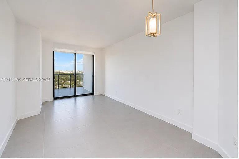 Open-concept living space featuring large-format tile flooring, a geometric metallic pendant light, and floor-to-ceiling sliding glass doors opening to a private balcony