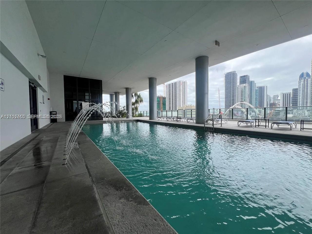 Covered swimming pool featuring water fountains, concrete decking, and structural support columns