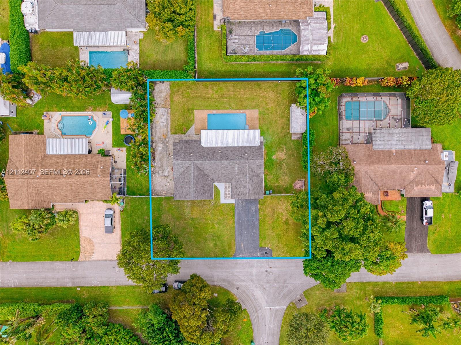 Aerial perspective of a property featuring an asphalt driveway, a shingled roof, a rectangular inground swimming pool, and a backyard area with mature landscaping