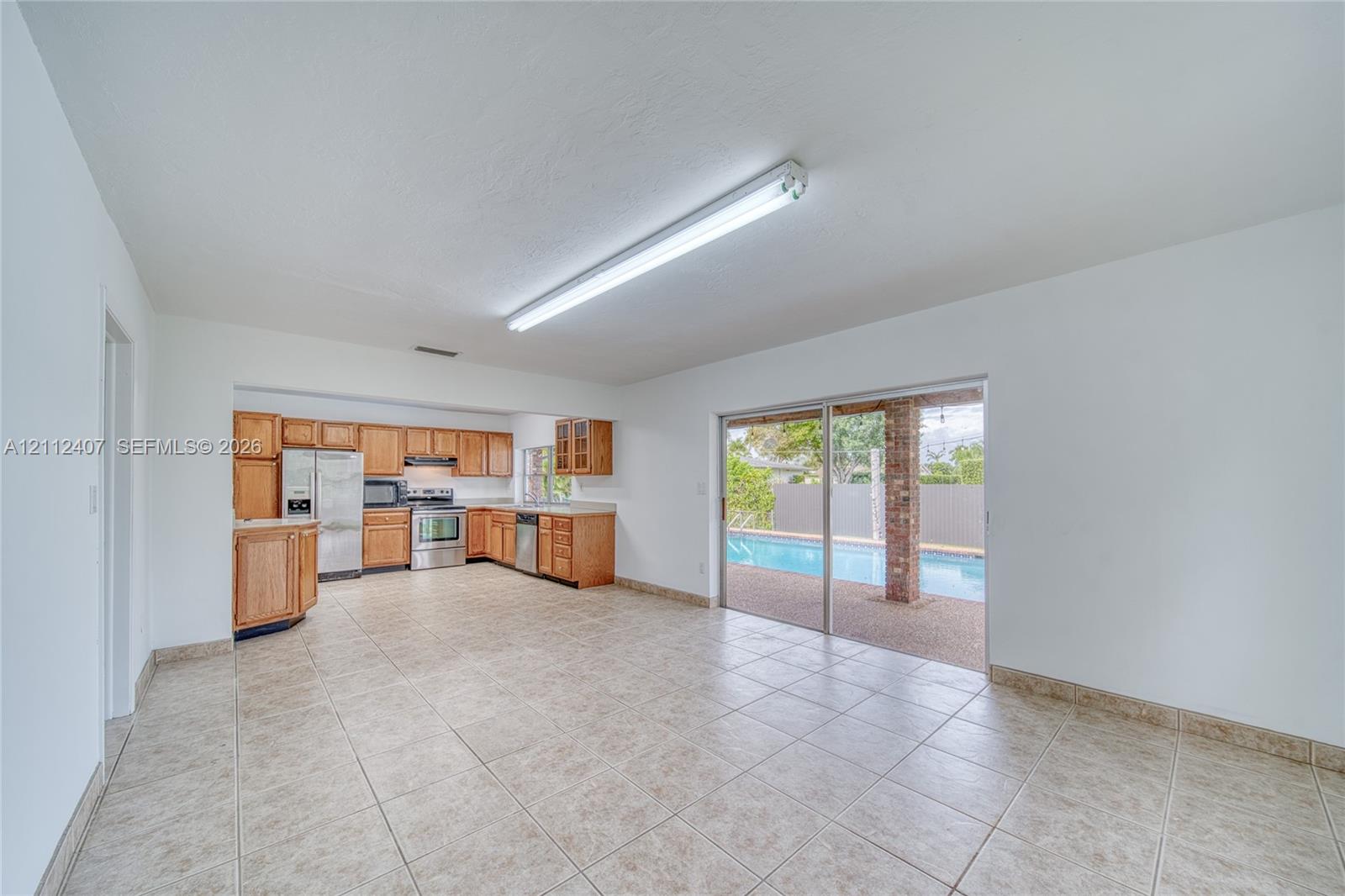 Kitchen area featuring wood cabinetry, stainless steel appliances, and tile flooring, with sliding glass doors opening to a pool and covered patio