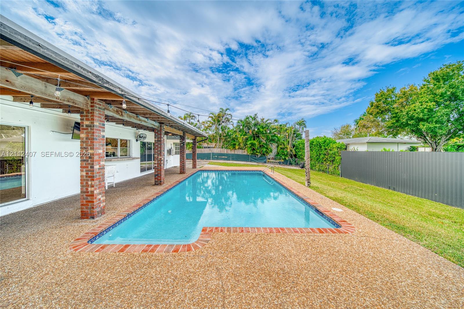 Covered outdoor patio with exposed wood beams and brick support columns, in-ground swimming pool with brick coping, and a fenced backyard Covered outdoor patio with exposed wood beams and brick support columns, in-ground swimming pool with brick coping, and a fenced backyard