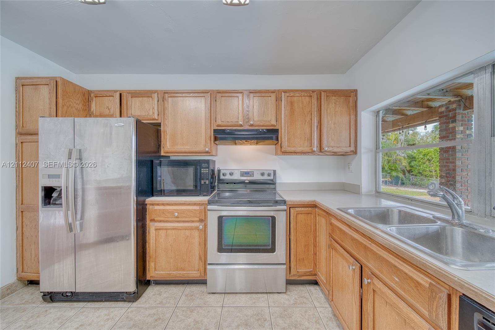 Kitchen featuring oak-finish cabinetry, stainless steel appliances, a double-basin stainless steel sink, and ceramic tile flooring