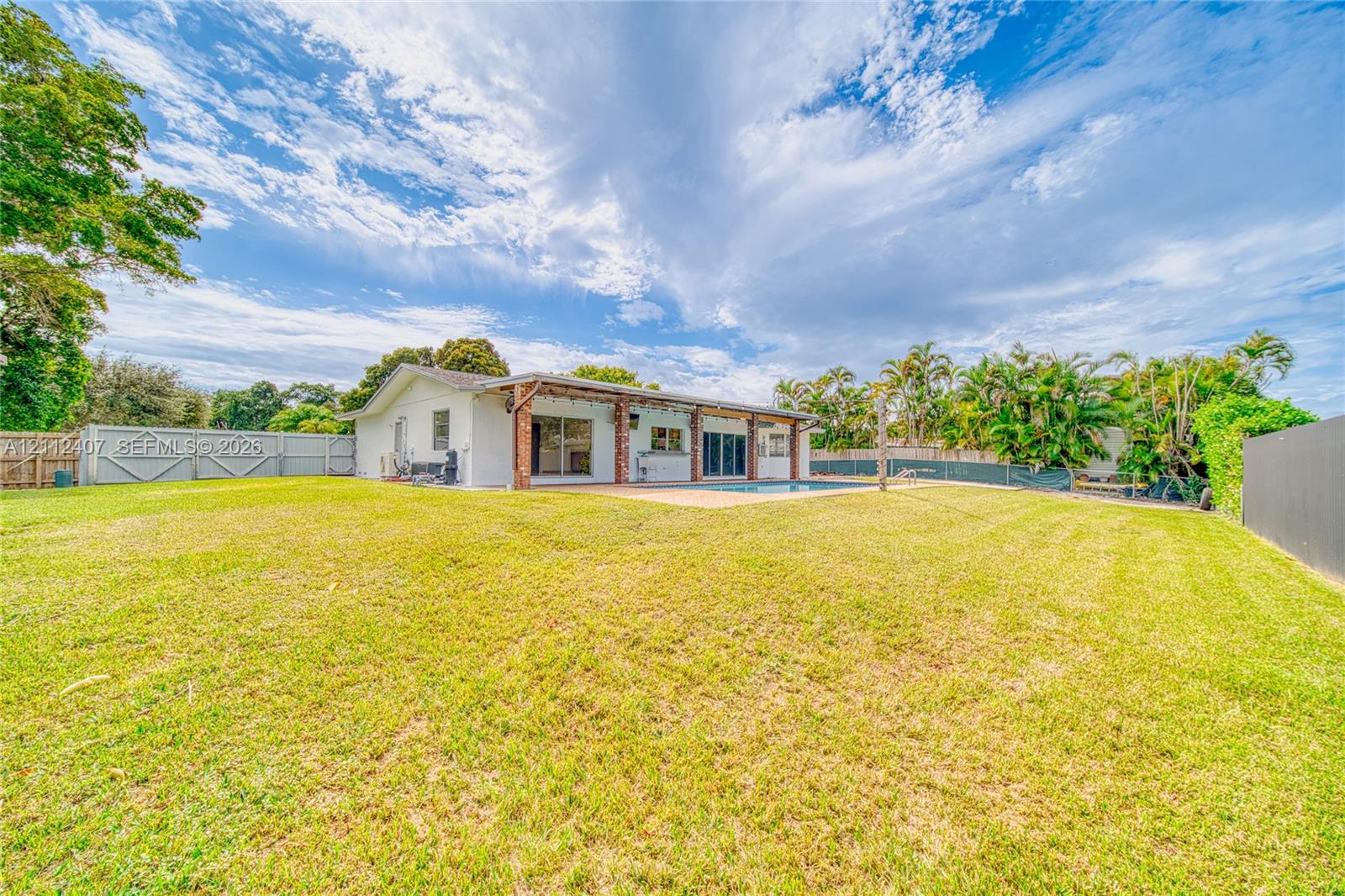 Expansive backyard featuring a large grass lawn, perimeter fencing, an in-ground pool, and a covered patio with brick structural supports Expansive backyard featuring a large grass lawn, perimeter fencing, an in-ground pool, and a covered patio with brick structural supports