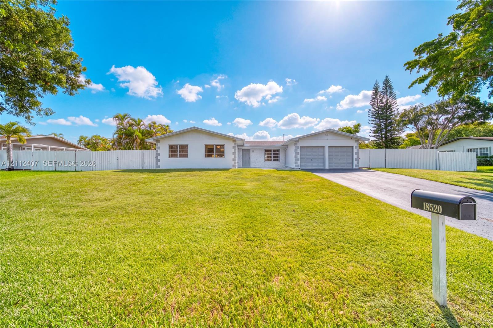 Single-story exterior featuring a painted masonry facade, two-car garage, asphalt driveway, and full perimeter vinyl fencing on a grass lot Single-story exterior featuring a painted masonry facade, two-car garage, asphalt driveway, and full perimeter vinyl fencing on a grass lot