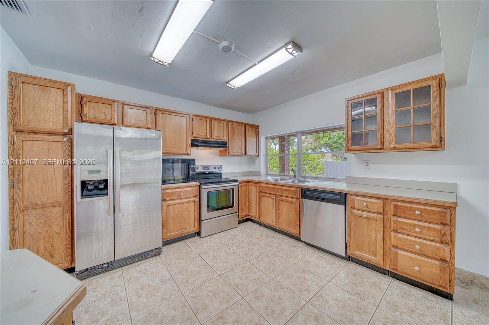 Kitchen featuring medium-tone wood cabinetry, solid-surface countertops, tile flooring, and a stainless steel appliance package including a refrigerator, dishwasher, and electric range Kitchen featuring medium-tone wood cabinetry, solid-surface countertops, tile flooring, and a stainless steel appliance package including a refrigerator, dishwasher, and electric range