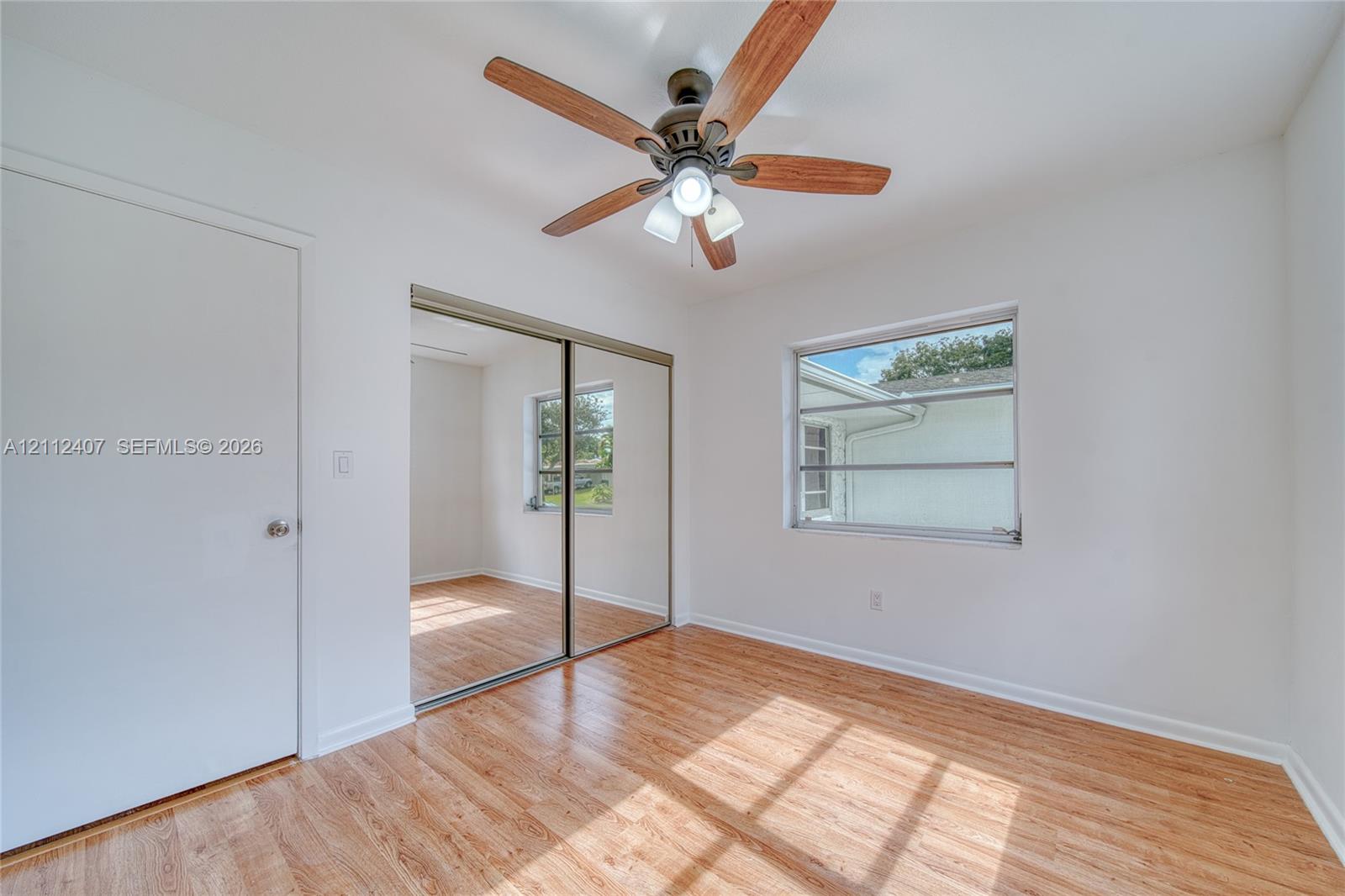 Room featuring wood-finish flooring, sliding mirror-panel closet doors, and a ceiling fan with integrated lighting