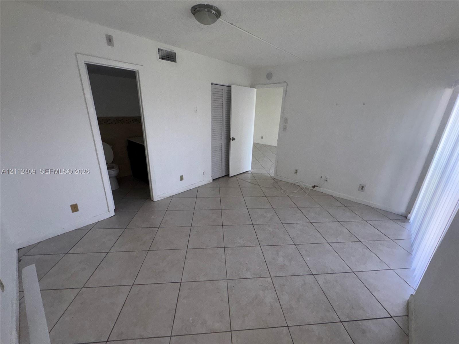 Interior space featuring neutral tile flooring, louvered closet doors, and flush-mount lighting