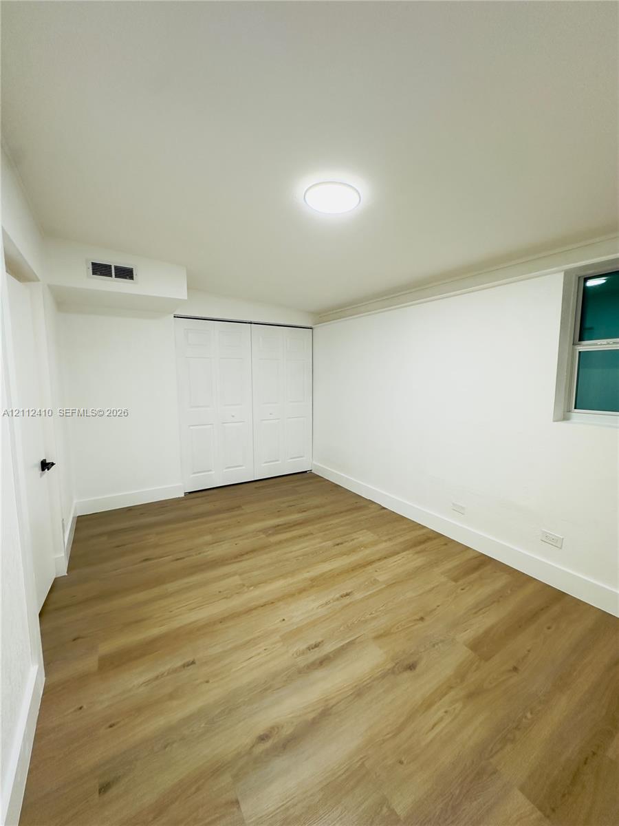 Room featuring wood-finish flooring, white walls, flush-mount ceiling lighting, and a dual-panel closet door