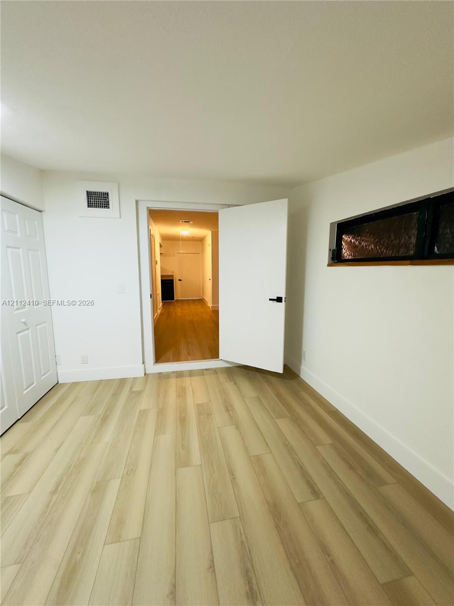 Room featuring wood-finish flooring, a white paneled closet door, a rectangular horizontal window with dark framing, and a white interior door with matte black hardware