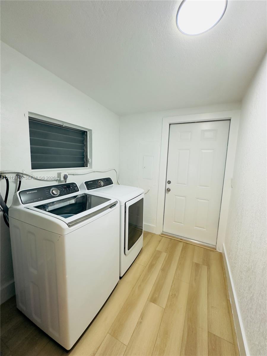 Utility room featuring wood-finish flooring, a jalousie-style window, and an exterior door with panel detailing