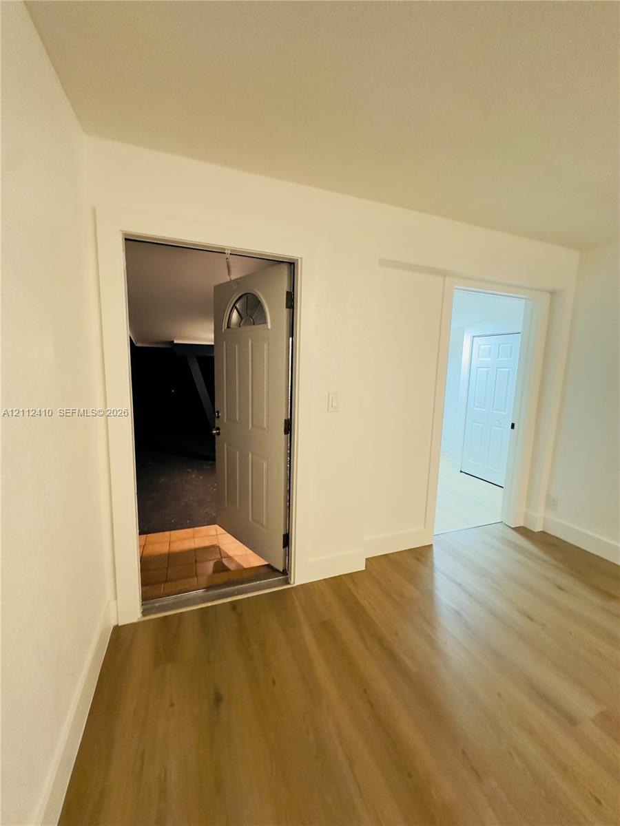 Interior featuring wood-finish flooring, white wall finishes, a six-panel exterior door with a semi-circle window insert, and a separate interior doorway with a double-panel closet door