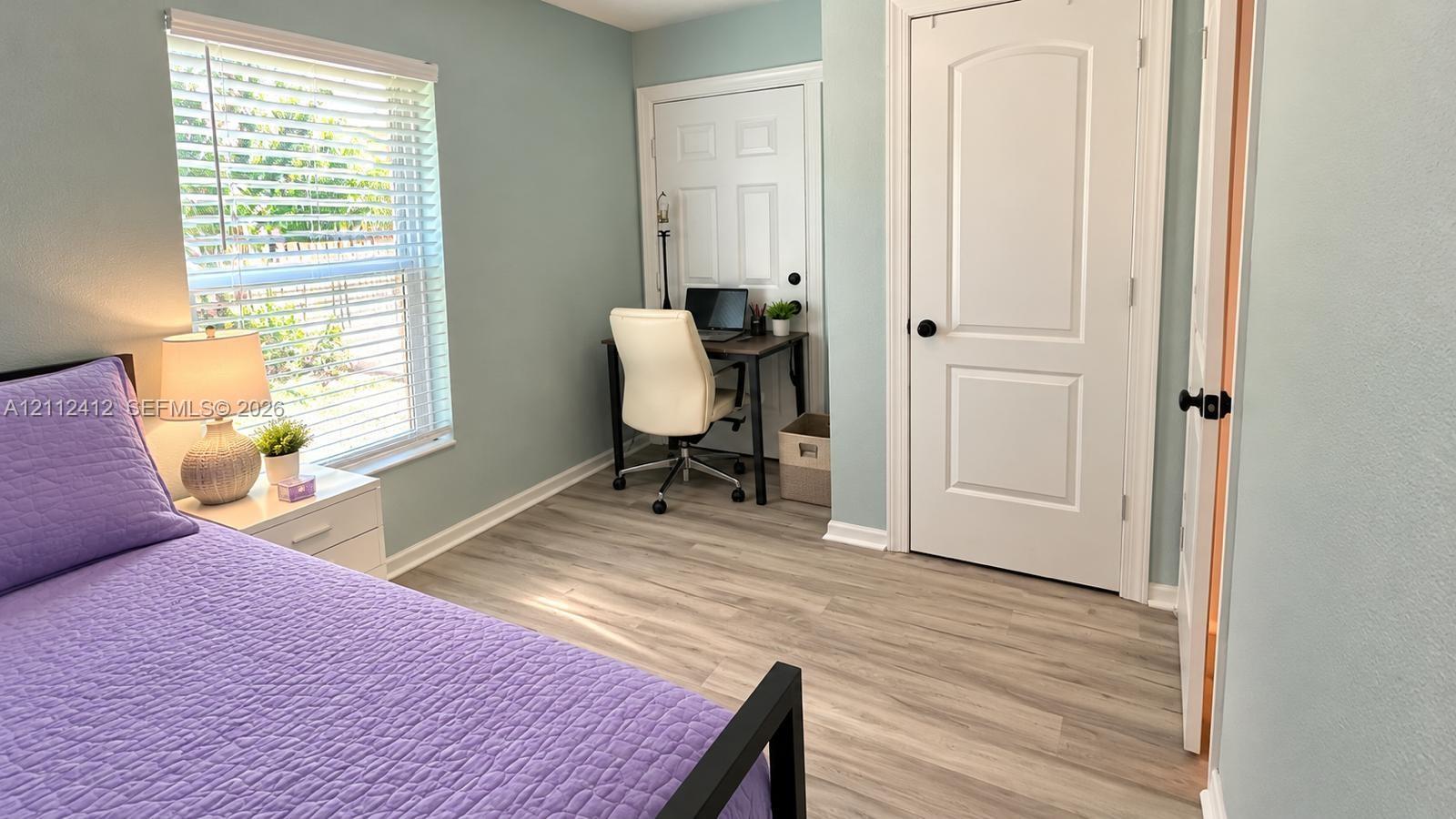 Room with wood-finish flooring, light-toned wall paint, a window with integrated blinds, and two interior doors featuring matte black hardware