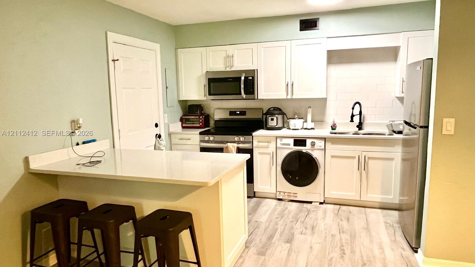 Kitchen featuring white cabinetry, wood-finish flooring, a quartz countertop peninsula, stainless steel appliances, and a matte black faucet Kitchen featuring white cabinetry, wood-finish flooring, a quartz countertop peninsula, stainless steel appliances, and a matte black faucet