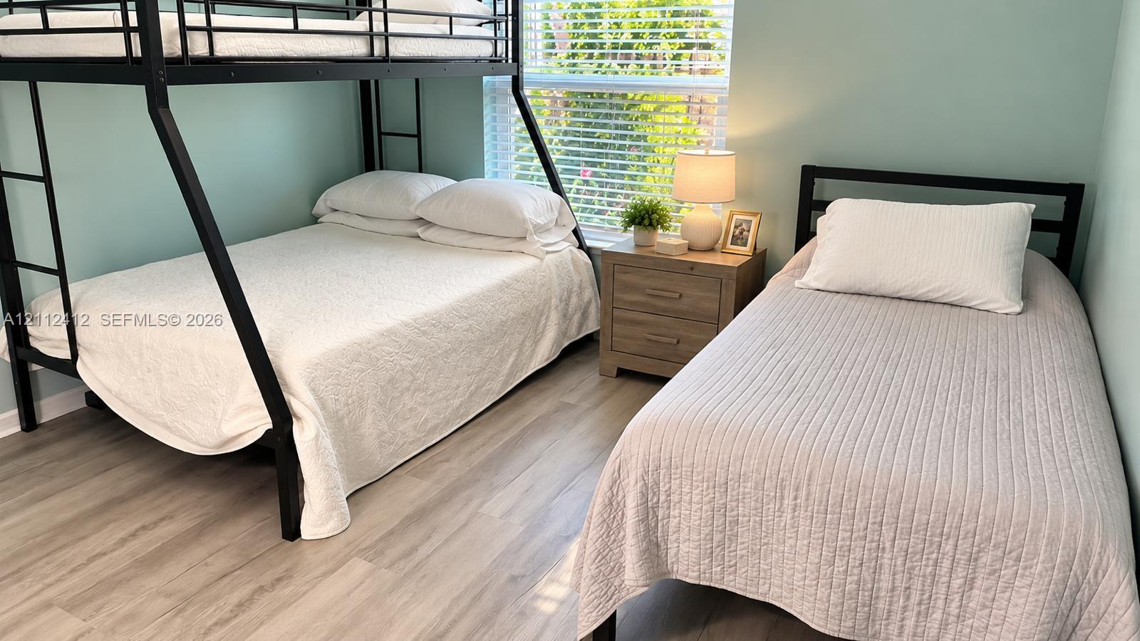 Bedroom featuring wood-finish flooring and a single-hung window with blinds Bedroom featuring wood-finish flooring and a single-hung window with blinds