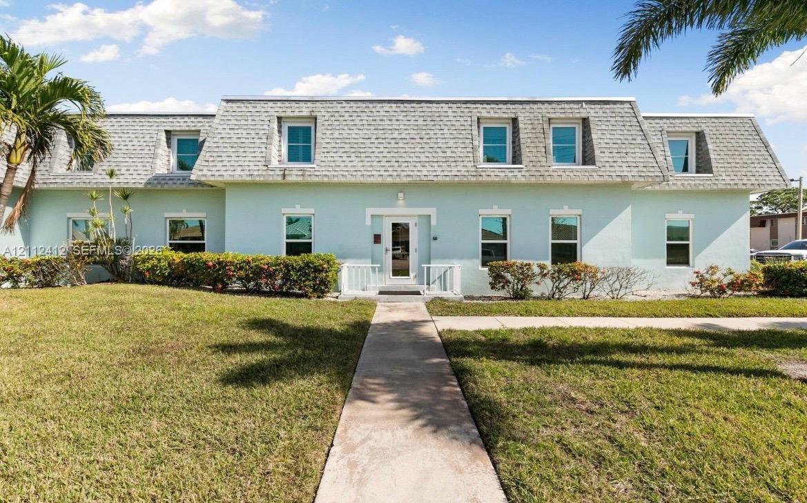 French Colonial inspired exterior featuring a mansard roofline, multi-pane windows, a central glass-panel door, and manicured landscaping