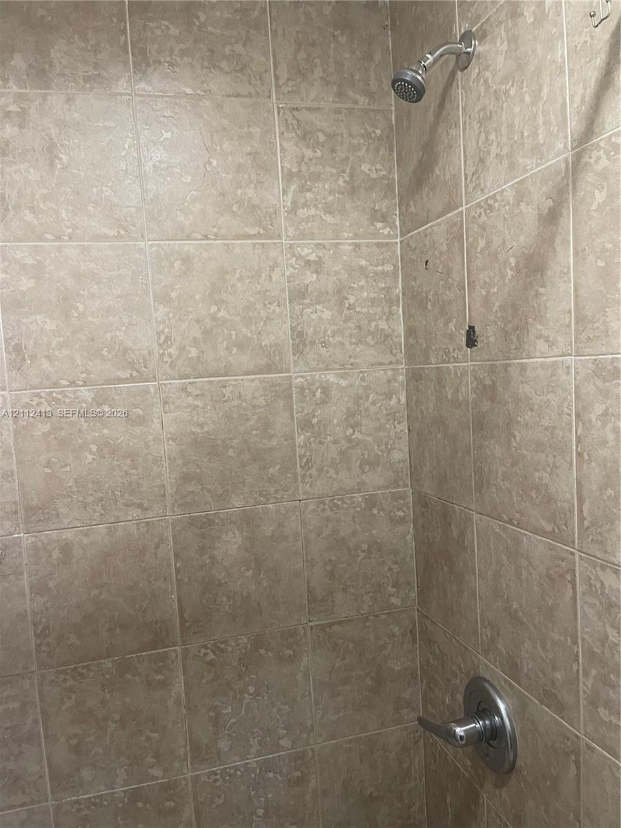 Shower enclosure featuring neutral-toned wall tiles, a metallic single-handle pressure balance valve, and a wall-mounted shower head