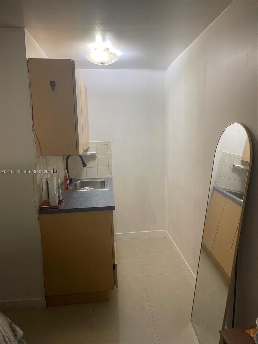 Compact kitchenette featuring light-finish cabinetry, a neutral solid-surface countertop, stainless steel drop-in sink, tile backsplash, and ceramic floor tiling