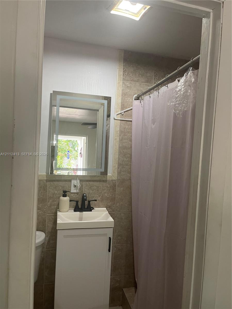 Bathroom featuring a vanity with a white basin, matte black faucet, illuminated wall mirror, and tile-surround shower area