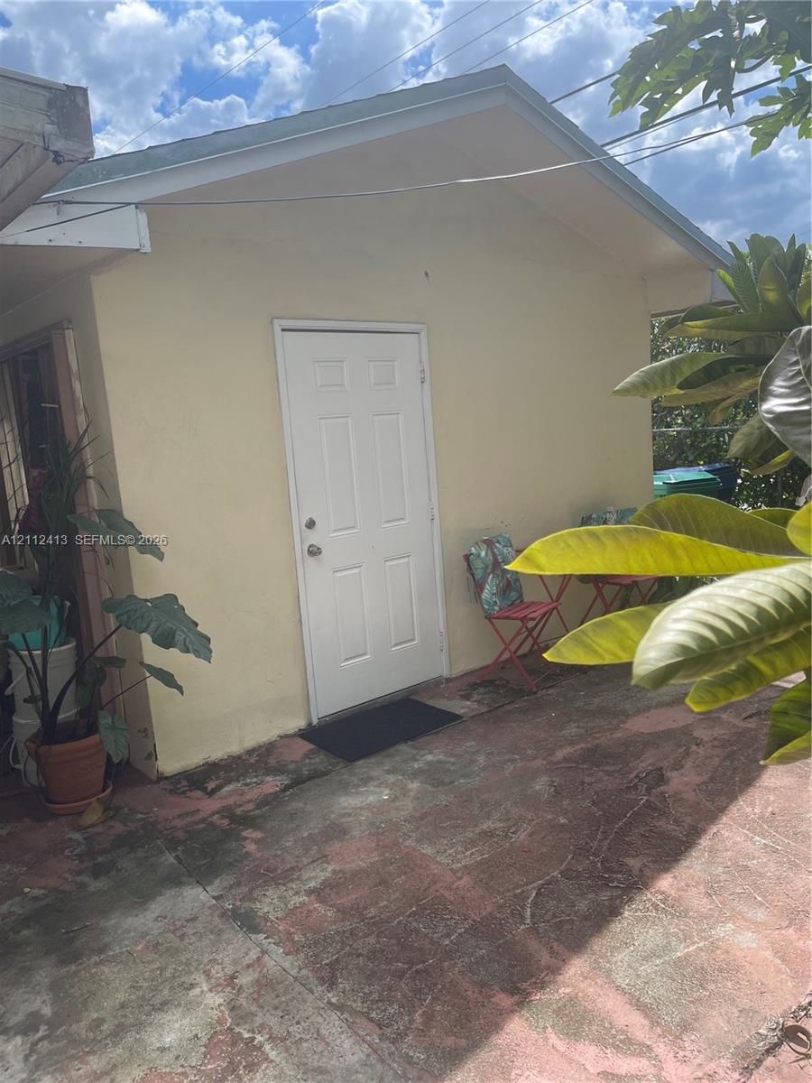 Gable-roof exterior with stucco siding, white panel door, and concrete patio surface