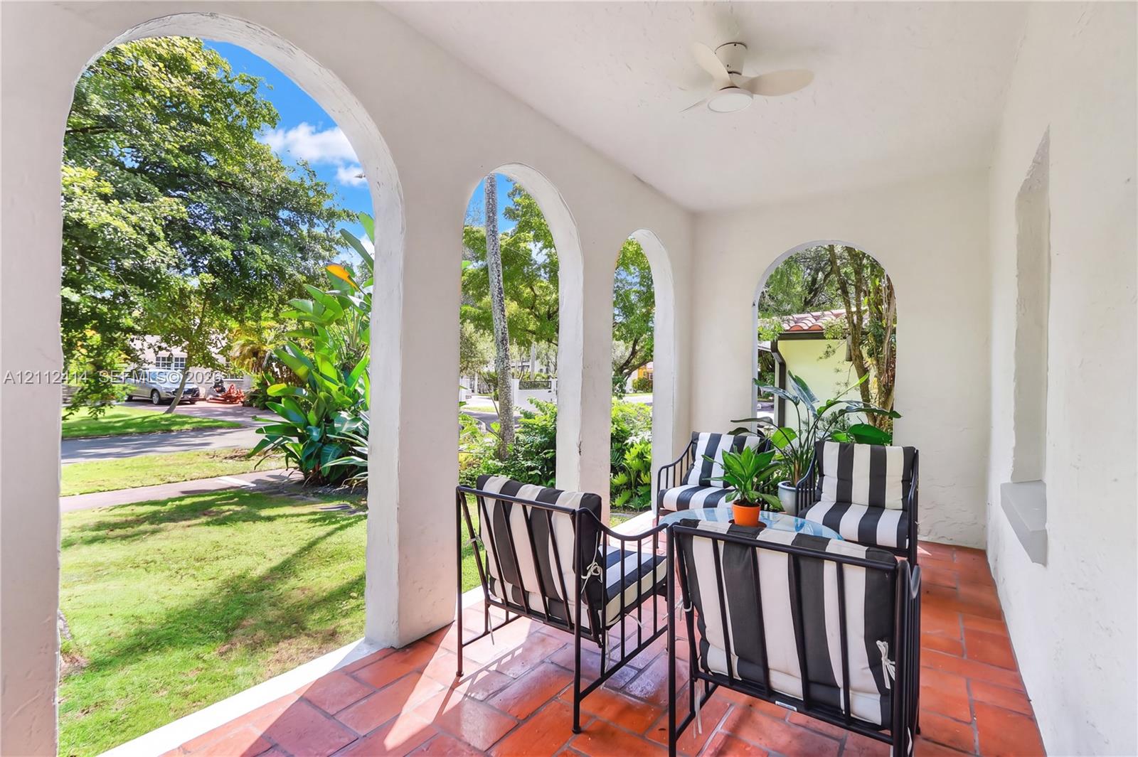 Covered porch featuring arched masonry openings, clay tile flooring, and a ceiling-mounted fan Covered porch featuring arched masonry openings, clay tile flooring, and a ceiling-mounted fan