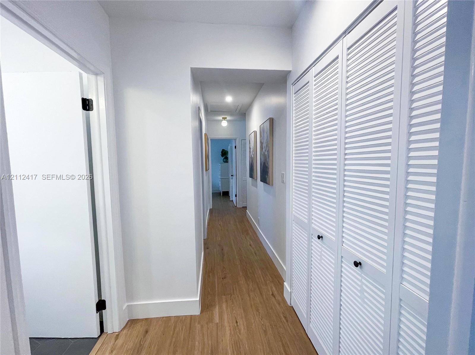 Hallway featuring wood-finish flooring, white louvered closet doors with matte black hardware, and recessed lighting