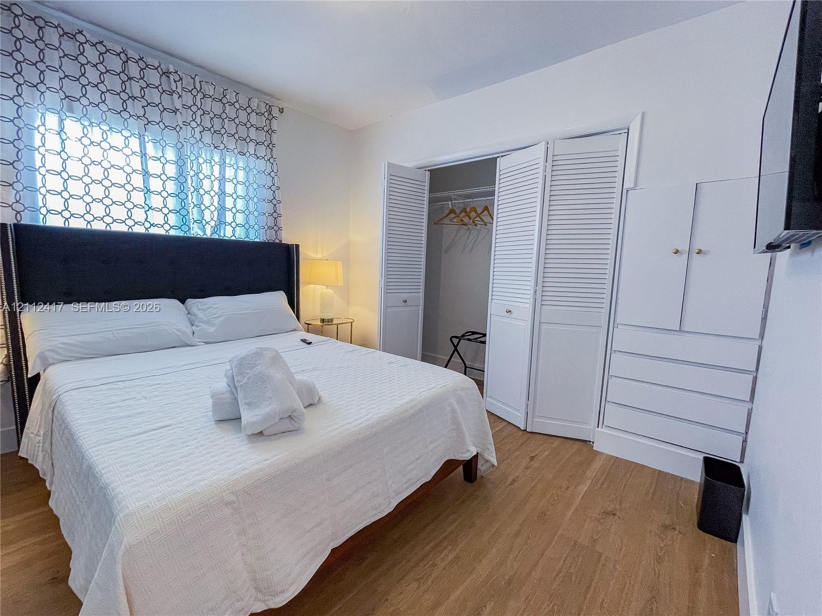 Wood-finish flooring, white louvered closet doors, and built-in white cabinetry with drawers