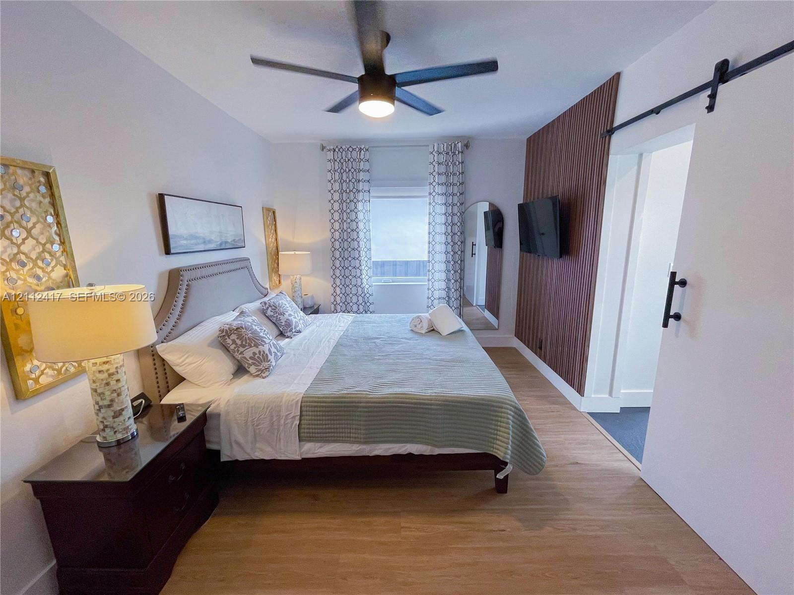 Wood-finish flooring, vertical wood-slat accent wall, sliding barn door, and a modern multi-blade ceiling fan with integrated lighting