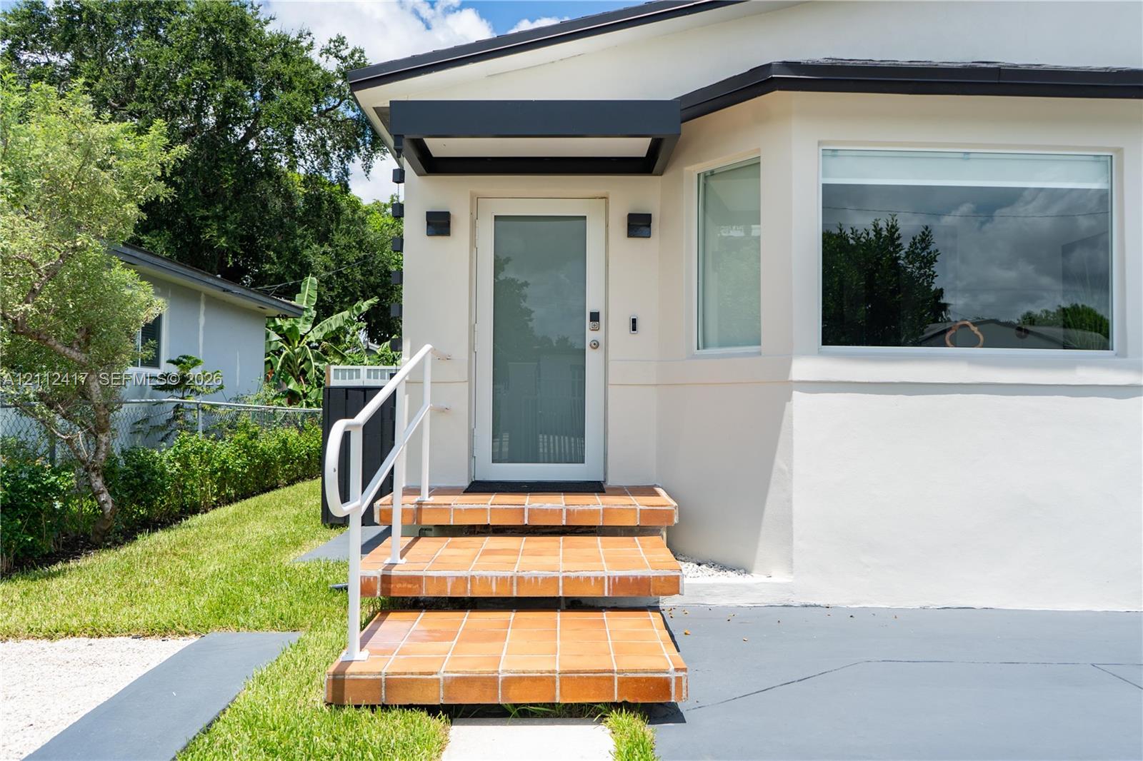 Exterior entrance featuring a glass-panel door, terra cotta tiled steps, a matte black awning, and white metal handrails
