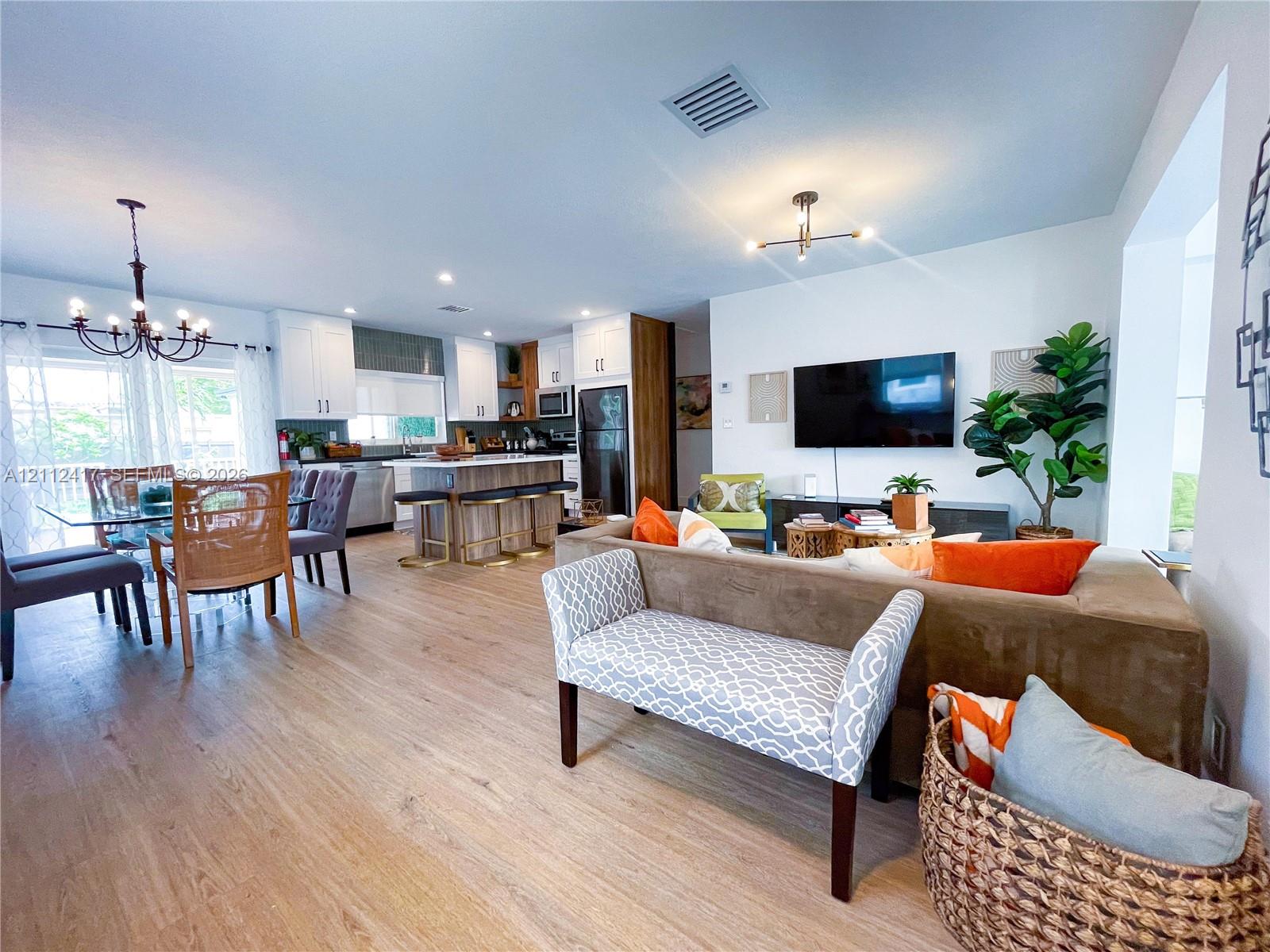 Open-concept interior featuring wood-finish flooring, kitchen island with built-in cabinetry, shaker-style cabinets, and decorative multi-arm chandelier lighting