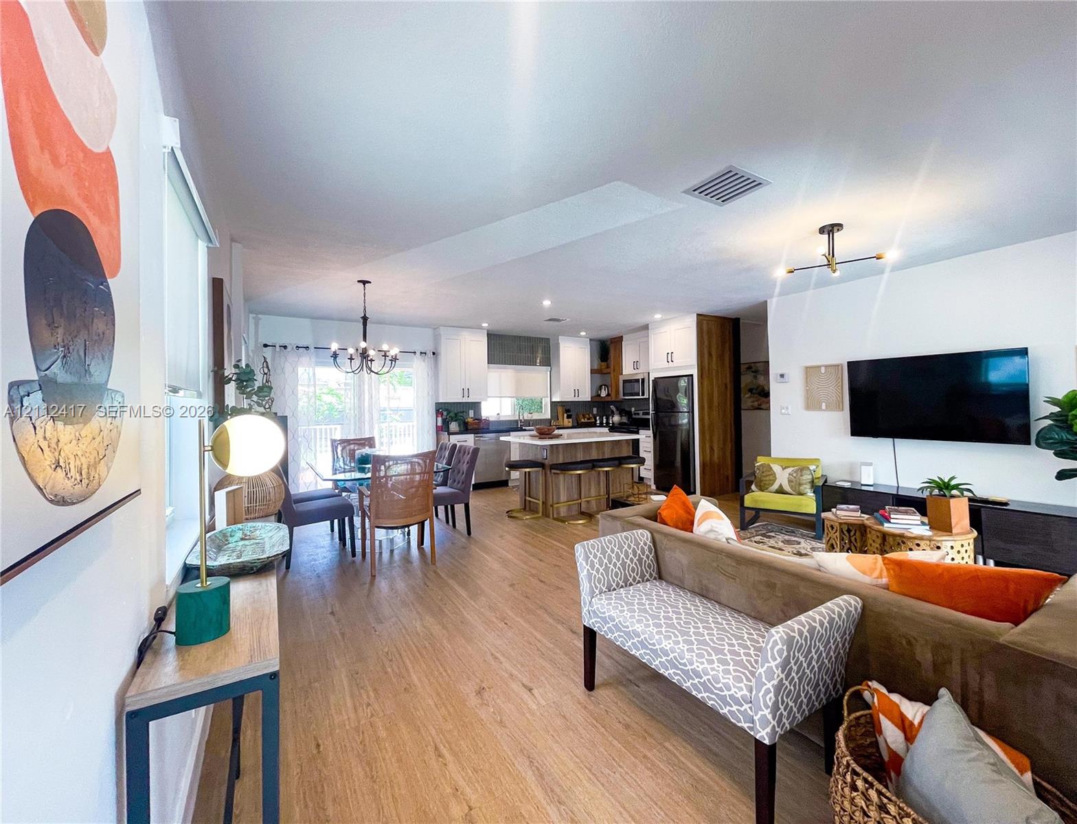 Open-concept interior featuring wood-finish flooring, white cabinetry, a center island with bar seating, and contemporary multi-arm overhead lighting