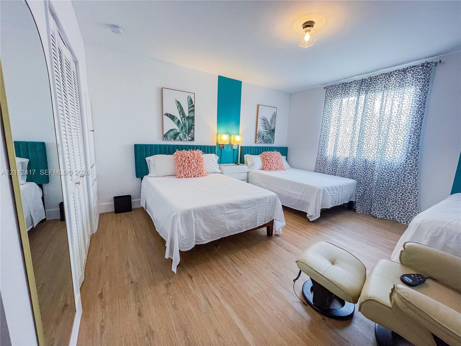 Wood-finish flooring, floor-to-ceiling mirrored closet doors with louvered panels, and flush-mount ceiling lighting