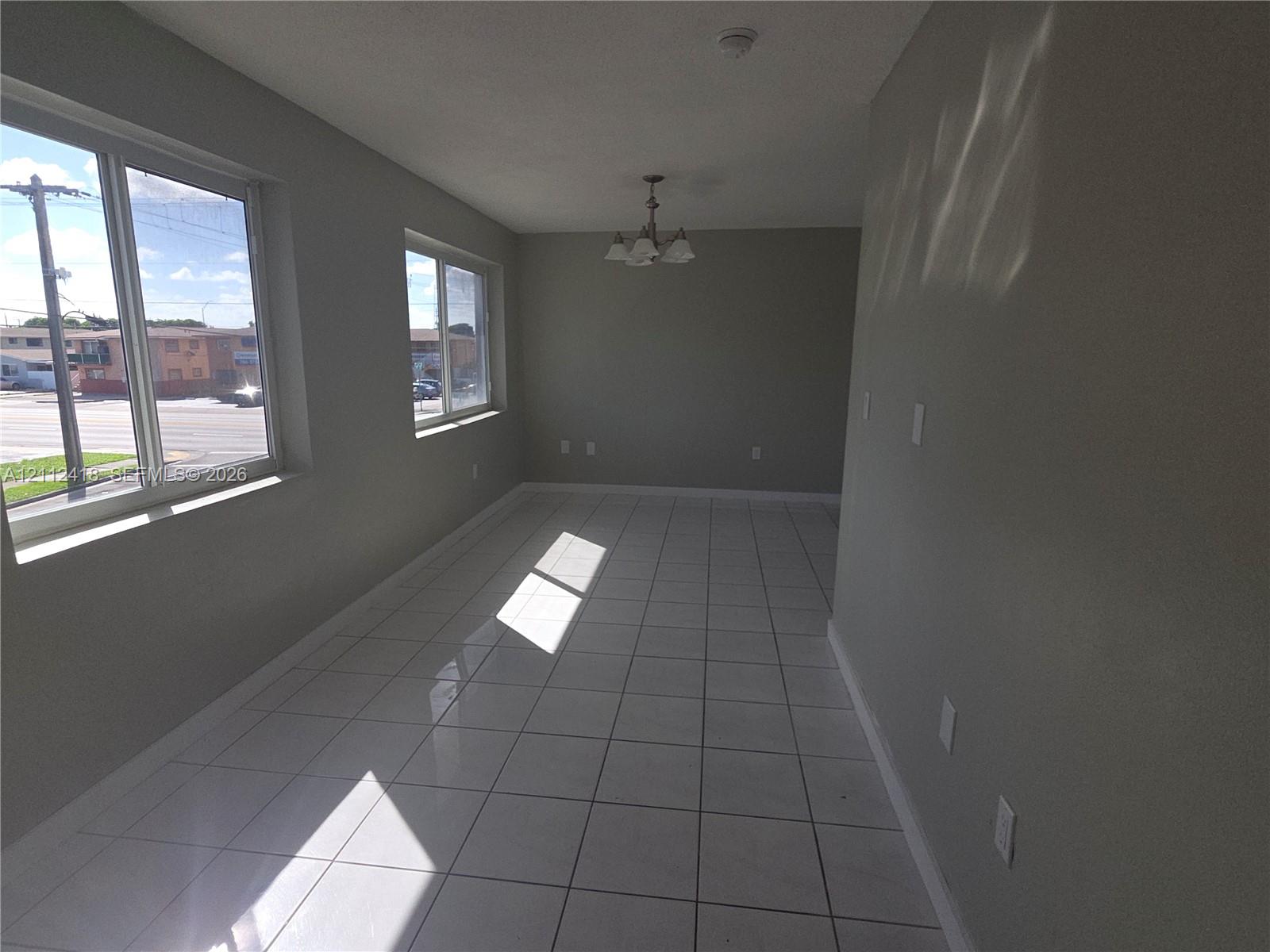 Interior space featuring large-format ceramic tile flooring, neutral wall tones, multi-pane windows, and a traditional tiered ceiling fixture