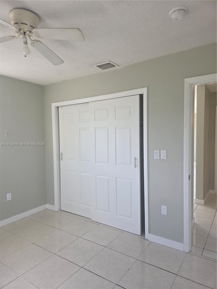 Neutral-toned interior space featuring light-colored tile flooring, six-panel sliding closet doors, and a ceiling-mounted fan with integrated lighting Neutral-toned interior space featuring light-colored tile flooring, six-panel sliding closet doors, and a ceiling-mounted fan with integrated lighting