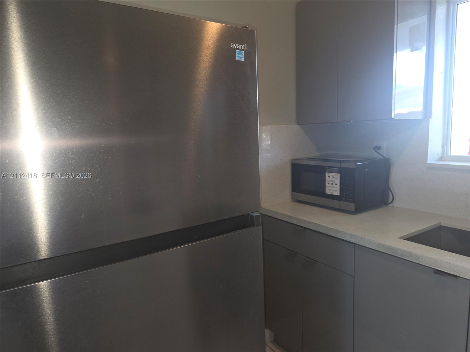 Stainless steel refrigerator, gray flat-panel cabinetry, light-toned stone-finish countertop, and undermount sink Stainless steel refrigerator, gray flat-panel cabinetry, light-toned stone-finish countertop, and undermount sink