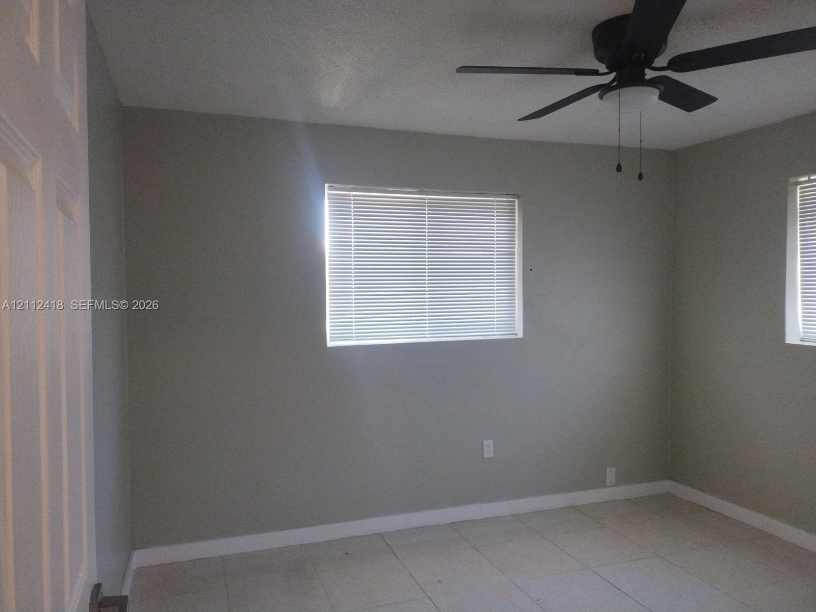 Neutral-toned walls featuring tile flooring, horizontal window blinds, and a multi-blade ceiling fan with integrated lighting Neutral-toned walls featuring tile flooring, horizontal window blinds, and a multi-blade ceiling fan with integrated lighting