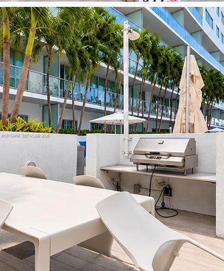 Outdoor terrace featuring a built-in stainless steel grill, stone-finish countertop, tile flooring, and perimeter privacy walls