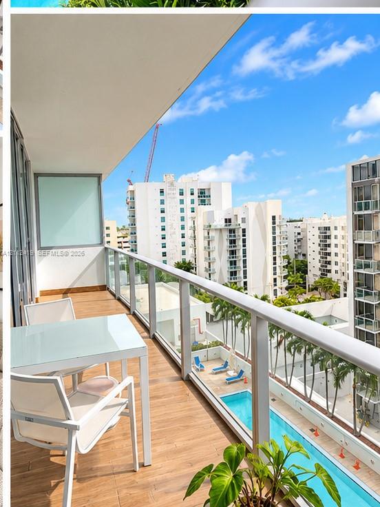 Covered balcony featuring wood-finish flooring, glass panel railings, and an elevated perspective of the community swimming pool