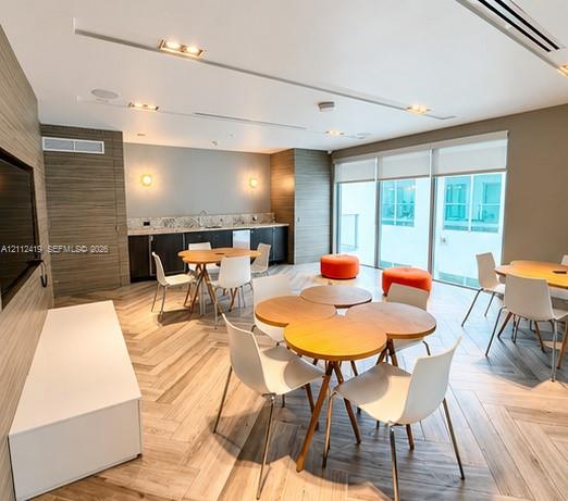 Herringbone wood-finish flooring, built-in wet bar with stone countertop, horizontal wood-texture wall paneling, and floor-to-ceiling windows with integrated roller shades