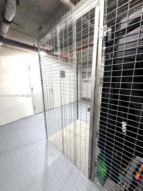 Secure storage unit featuring metal mesh walls, a locking door mechanism, and painted concrete flooring