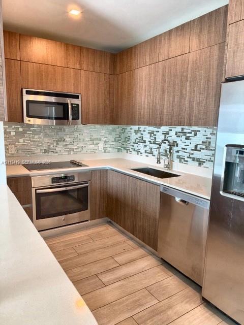 Contemporary kitchen featuring flat-panel wood-finish cabinetry, quartz countertops, mosaic glass tile backsplash, stainless steel appliances, and wood-finish tile flooring