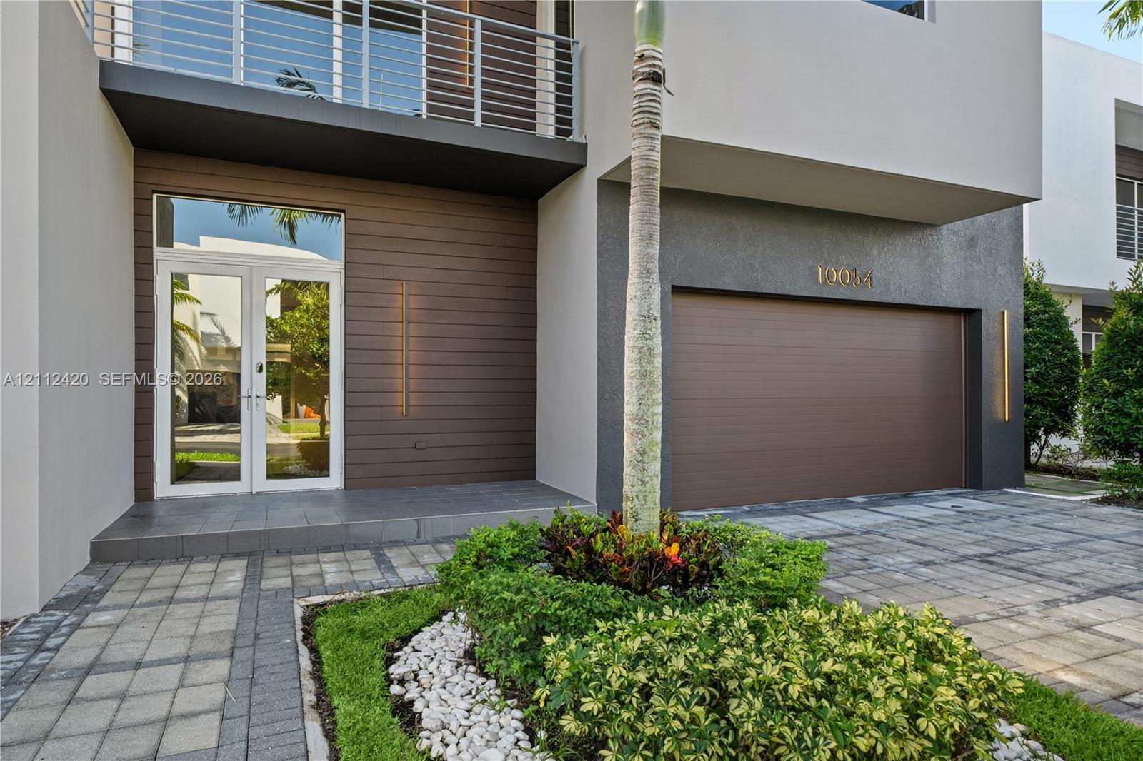 Contemporary exterior featuring a horizontal wood-plank facade, second-story balcony with metal railing, double-door entryway, and paver driveway Contemporary exterior featuring a horizontal wood-plank facade, second-story balcony with metal railing, double-door entryway, and paver driveway
