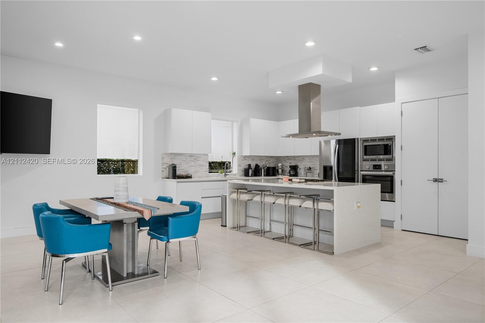Kitchen featuring flat-panel cabinetry, a quartz-topped center island with integrated seating, stainless steel appliances, a chimney-style range hood, and tile flooring