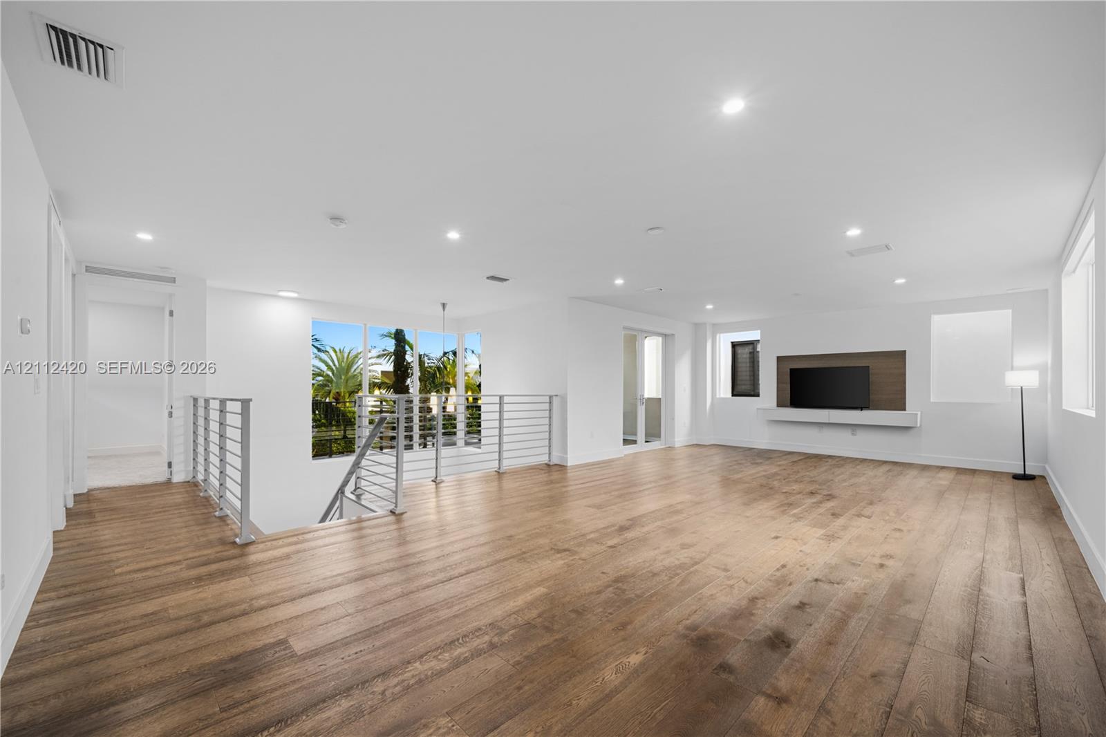 Open-concept interior featuring wood-finish flooring, recessed lighting, a built-in media console, and a horizontal metal-railing staircase