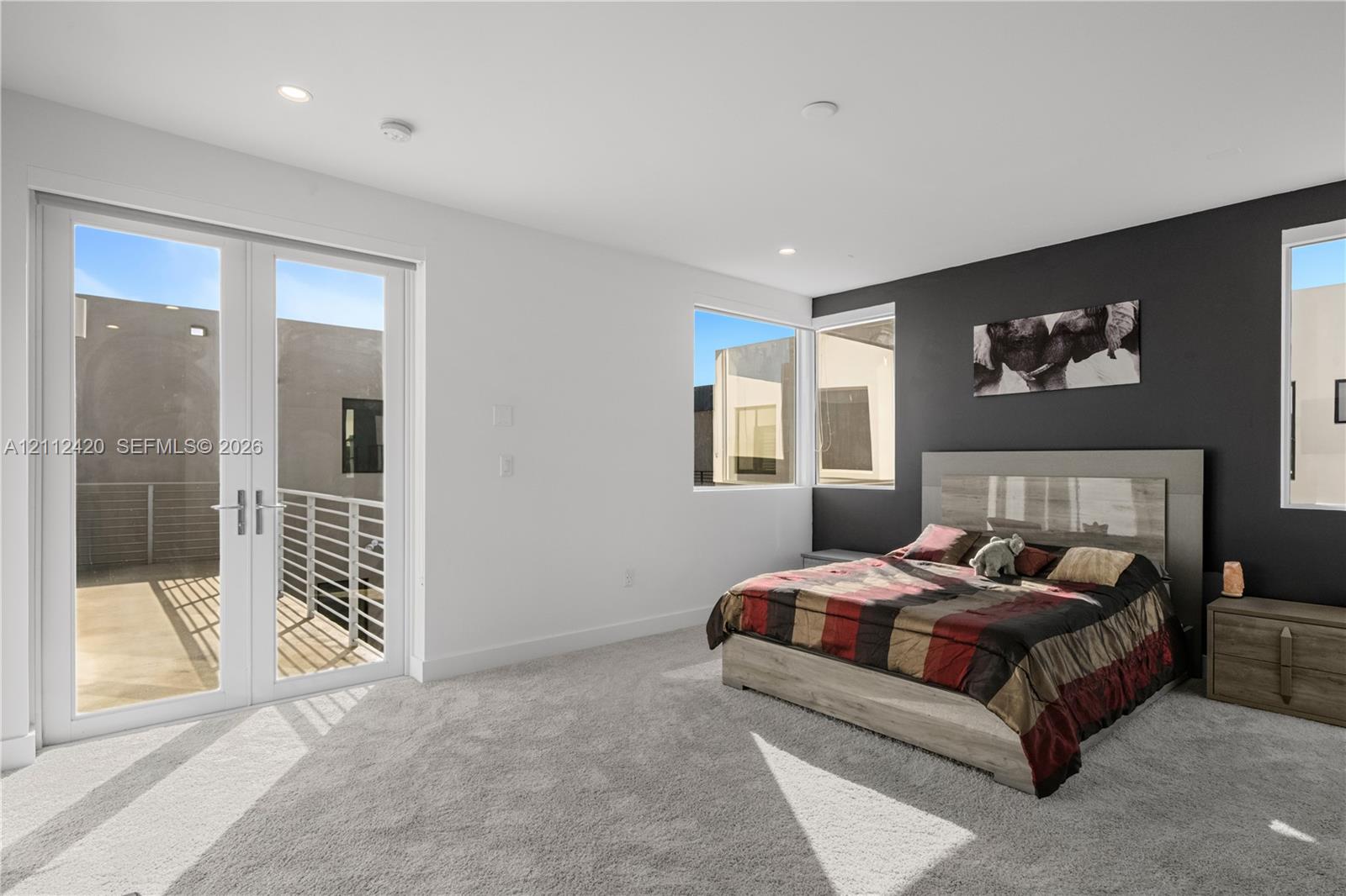 Interior space featuring recessed lighting, carpeted flooring, a dark accent wall, and double-glass doors opening to an exterior balcony with a metal railing