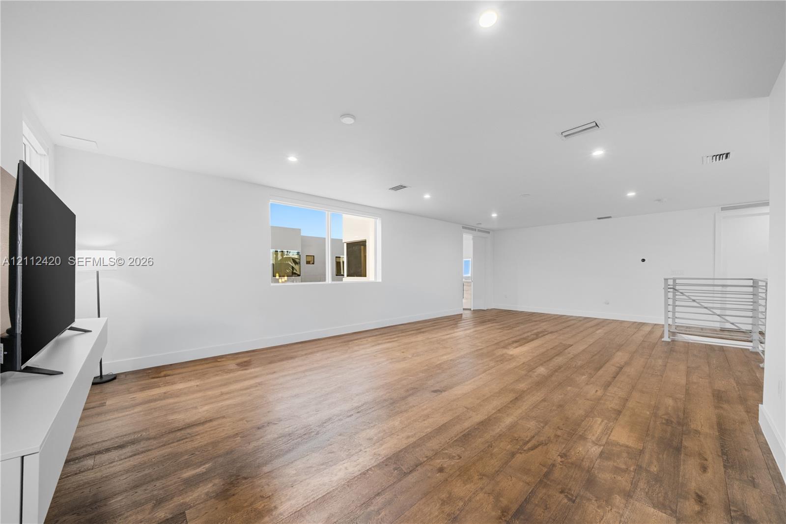 Spacious interior featuring wood-finish flooring, recessed lighting, and a metal stair railing